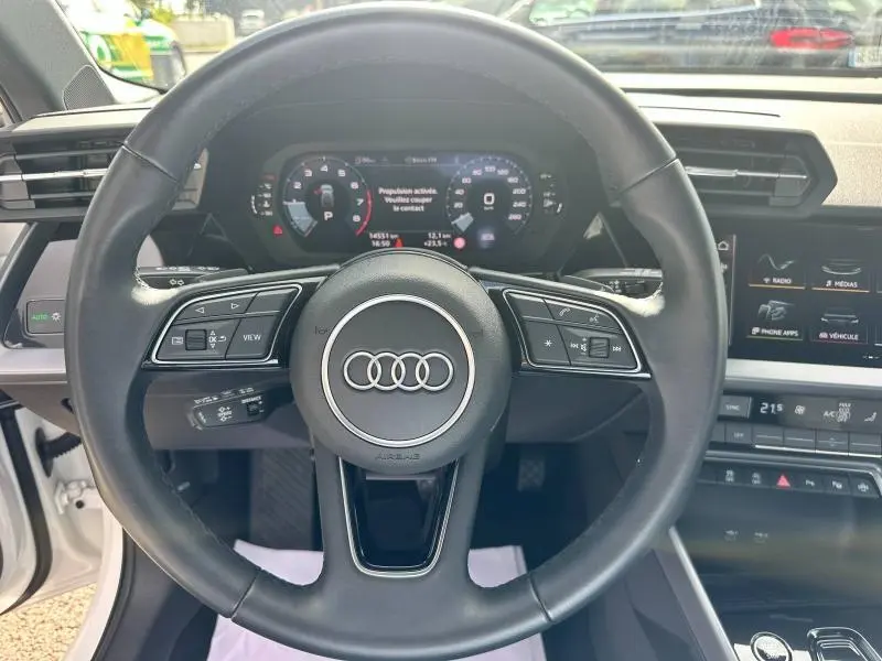 Vue centrée sur le volant cuir multifonction d'une Audi A3 Sportback 2024, tableau de bord digital et écran tactile visibles.