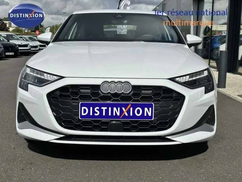 Vue frontale d'une Audi A3 Sportback blanche Arkona avec calandre noire hexagonale et logo Distinxion sur plaque avant.