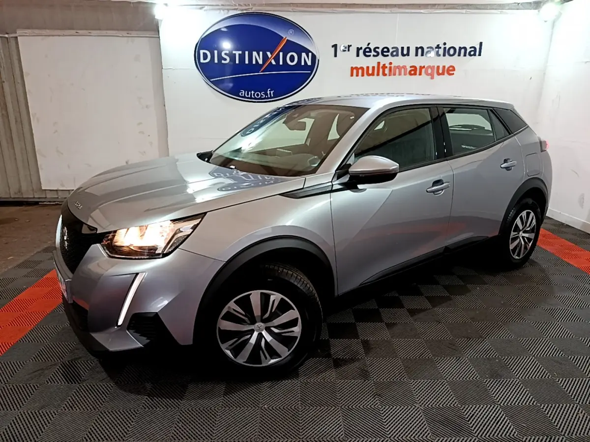 Peugeot 2008 BlueHDi 110 gris clair vue 3/4 avant droit avec phares allumés en intérieur showroom