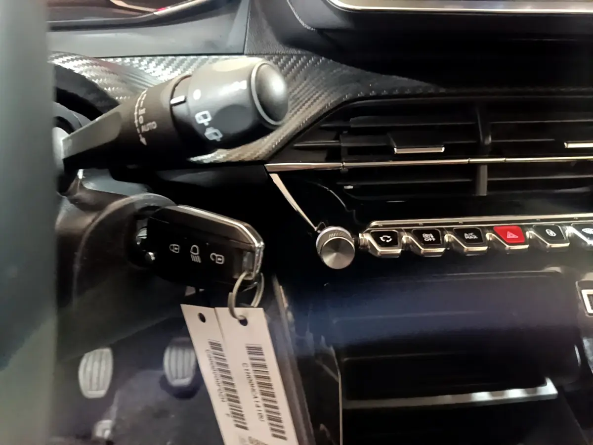 Gros plan sur la clé et la console centrale noire brillante du Peugeot 2008 gris clair, avec commandes et aérateurs visibles.