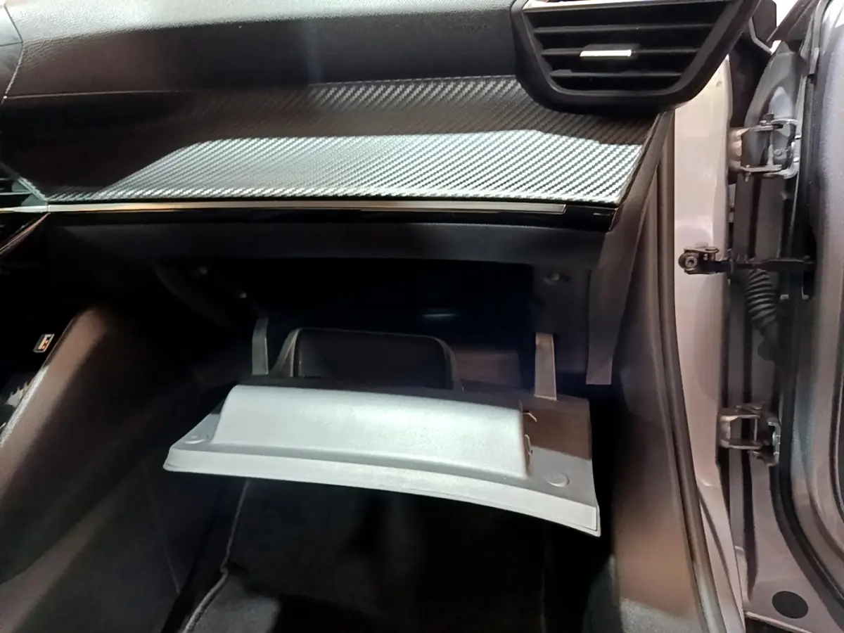 Vue intérieure côté passager du Peugeot 2008 gris clair 2022, boîte à gants ouverte sous tableau de bord noir à insert carbone.