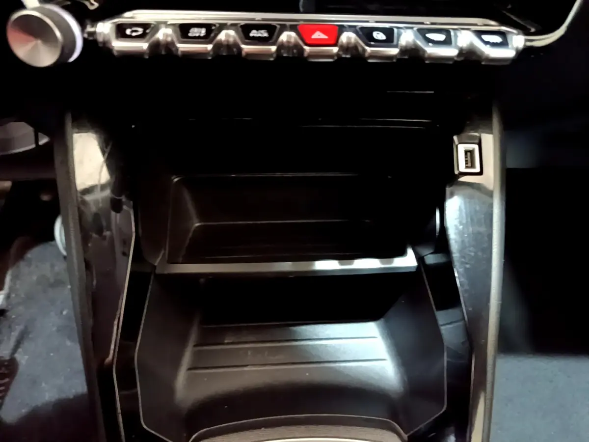 Gros plan sur la console centrale noire d'une Peugeot 2008 gris clair, avec rangements et port USB visible à droite.