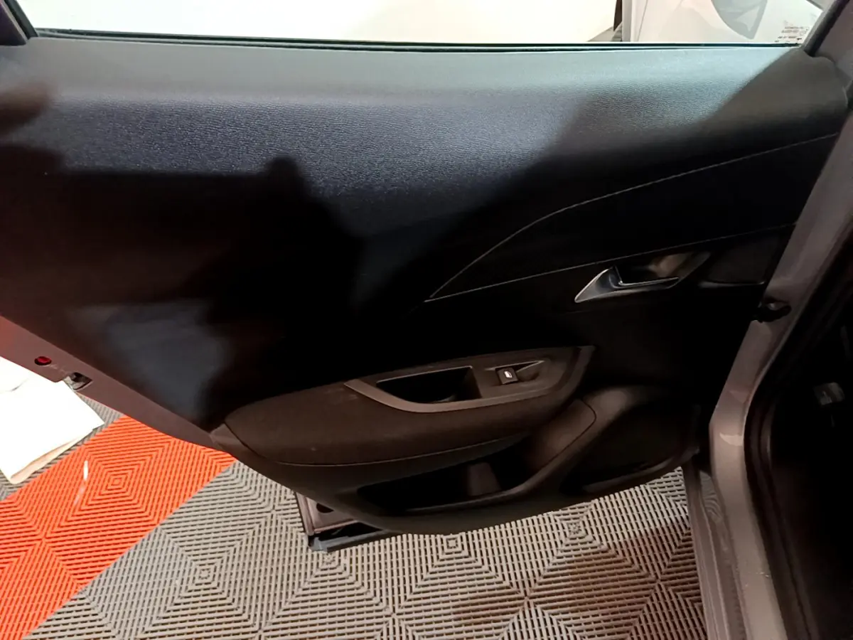 Vue rapprochée de la porte arrière droite intérieure du Peugeot 2008 gris clair, avec poignée et commande de vitre noire.
