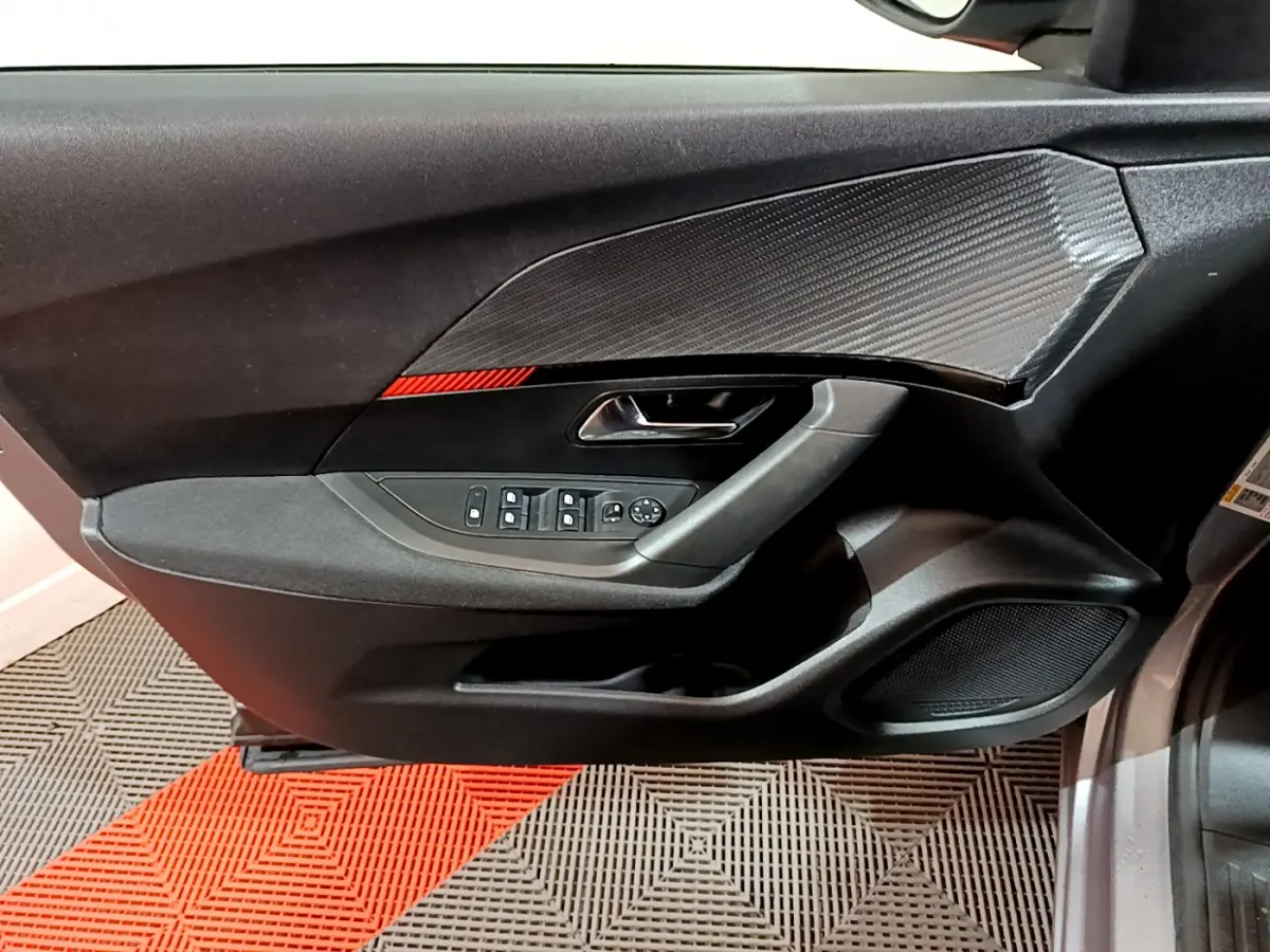 Intérieur côté gauche de la porte avant d'une Peugeot 2008 gris clair, avec commandes électriques et insert décoratif noir.