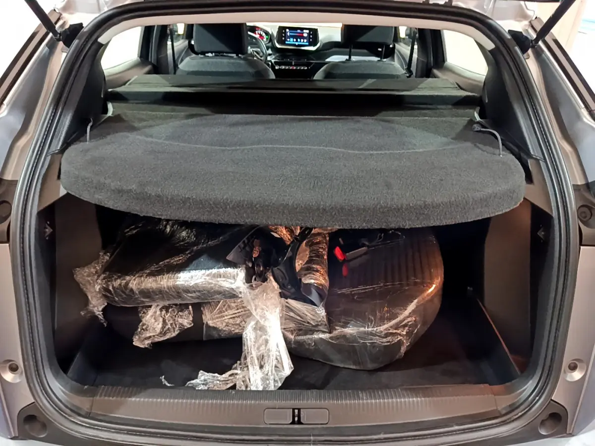 Coffre ouvert d’un Peugeot 2008 gris clair 2022, vue arrière montrant la tablette et un chargement emballé.