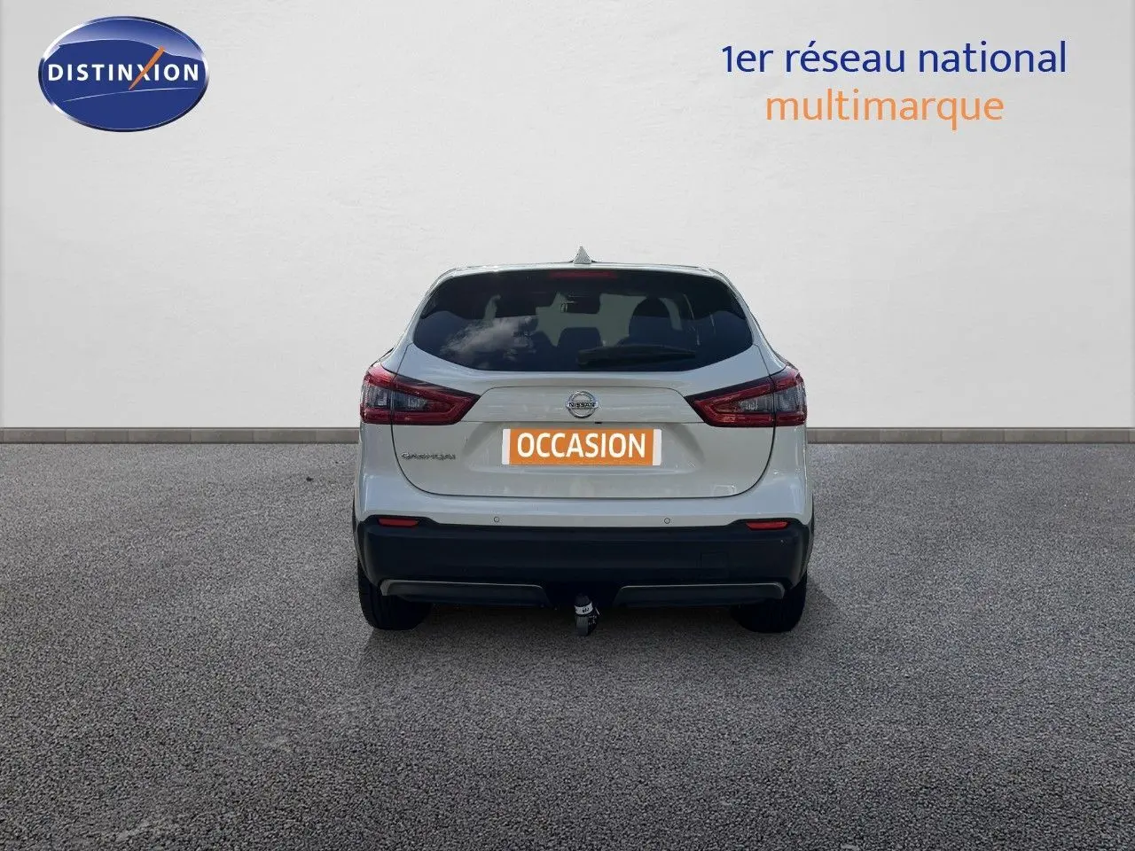 Vue arrière d'un Nissan Qashqai blanc nacré métal 2019 avec attelage et feux arrière allumés.