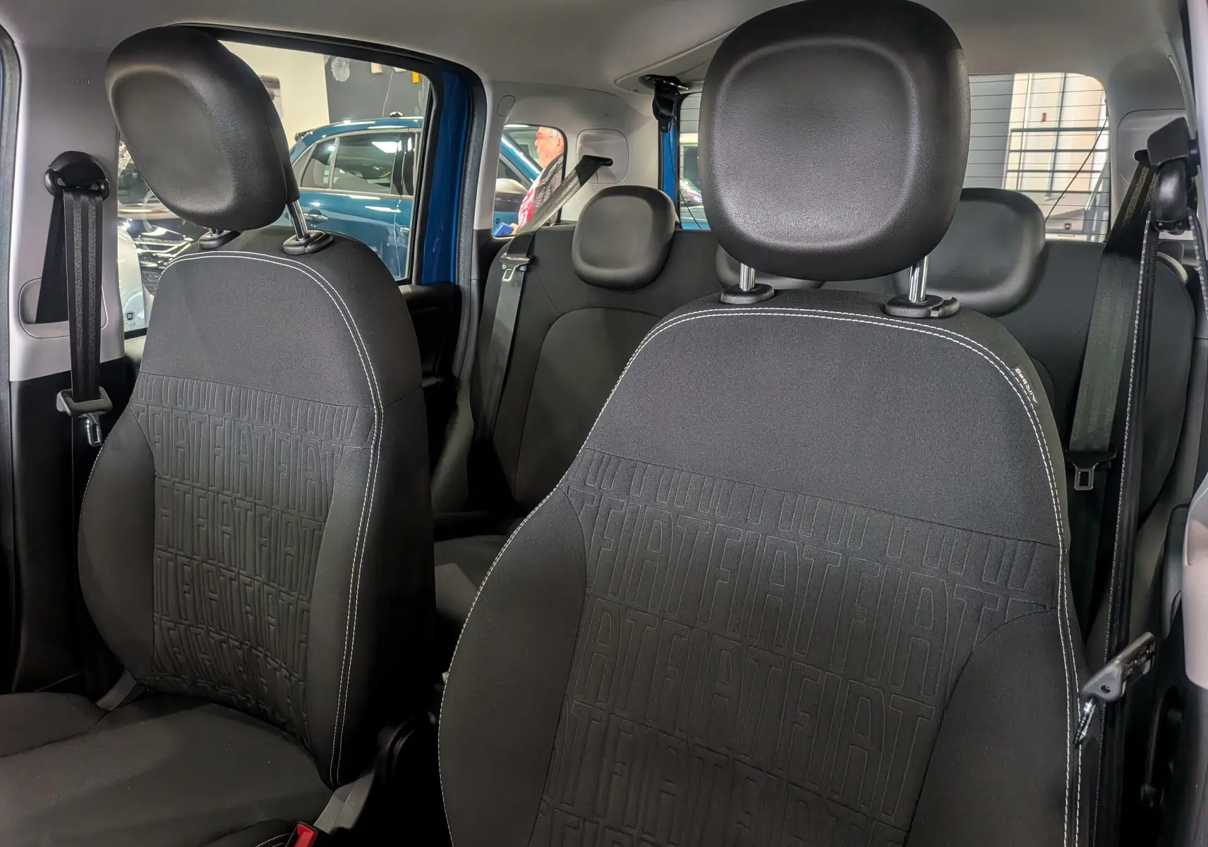 Intérieur de la Fiat Panda 2025 en Bleu Italia, vue des sièges avant en tissu noir avec motifs FIAT embossés.
