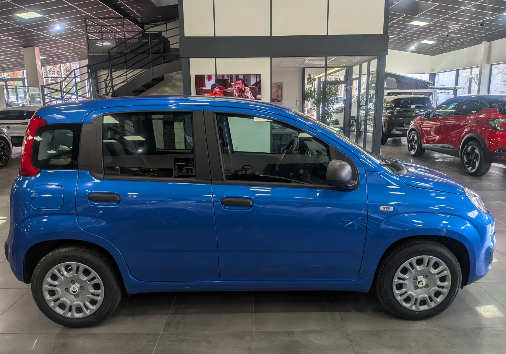 Profil côté droit de la Fiat Panda 1.0 Hybrid City 2025 en Bleu Italia, compacte et pratique en intérieur de showroom.