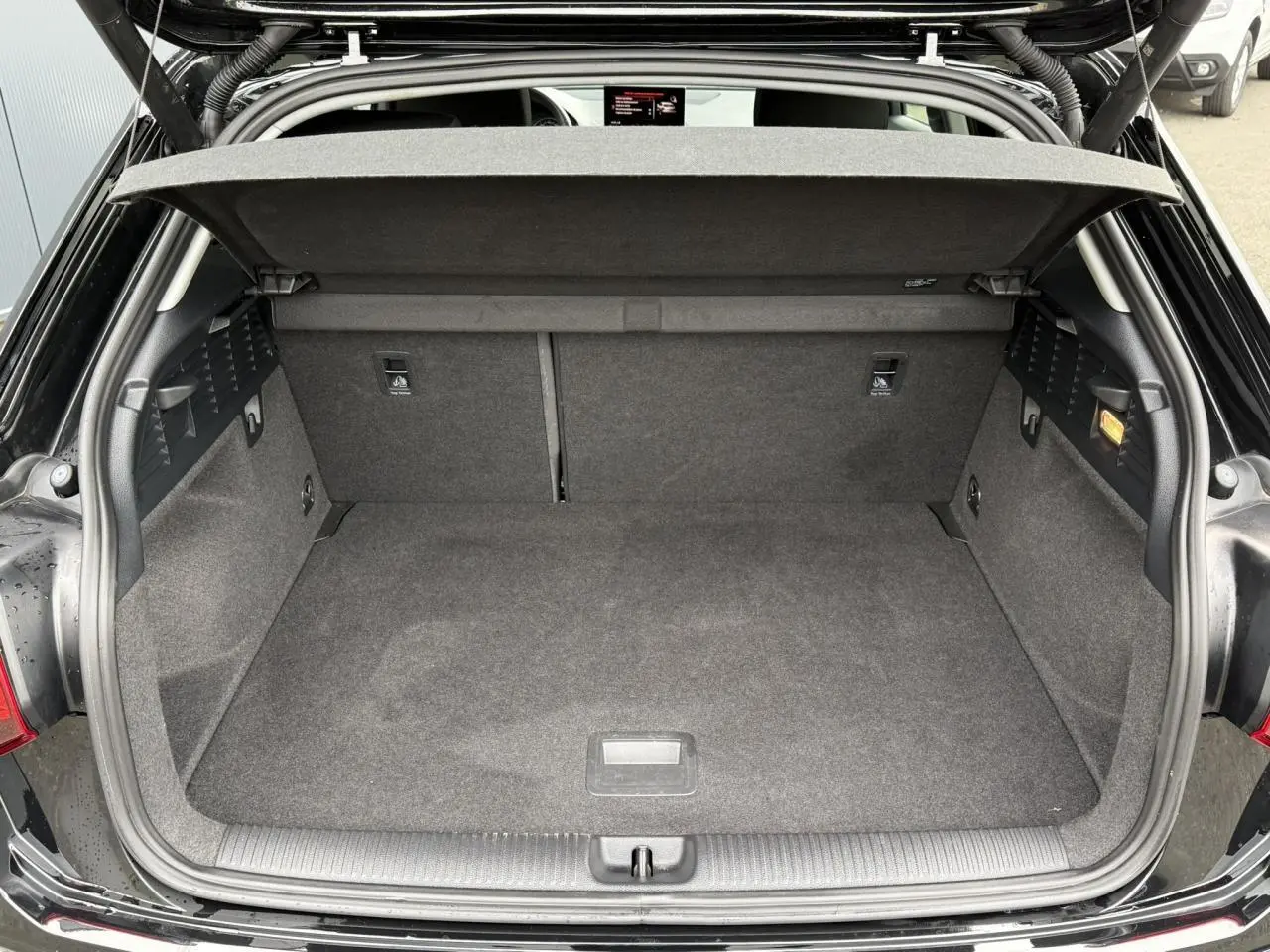 Coffre ouvert vu de l'arrière d'un Audi Q2 noir Mythe, montrant un espace de chargement propre et spacieux.