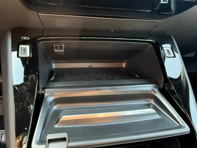 Gros plan sur la console centrale noire brillante du Peugeot 2008 Hybrid, montrant un rangement ouvert avec détails métalliques.