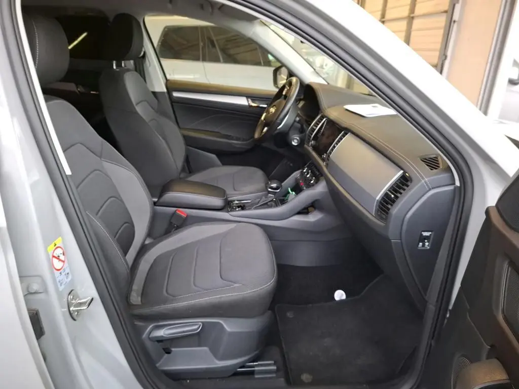 Intérieur avant du Skoda Kodiaq gris clair 2023, vue côté gauche montrant sièges tissu noirs et tableau de bord moderne.