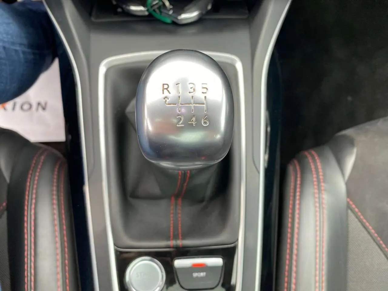 Le levier de vitesses manuel en aluminium de la Peugeot 308 GTi rouge, avec coutures rouges visibles sur la console.