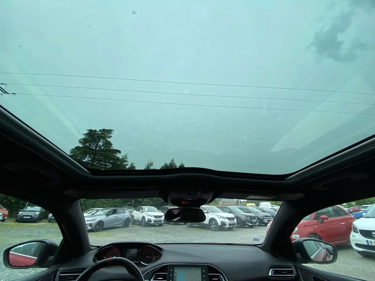 Vue intérieure avant du toit panoramique en verre de la Peugeot 308 GTi rouge avec tableau de bord et rétroviseur central visibles.