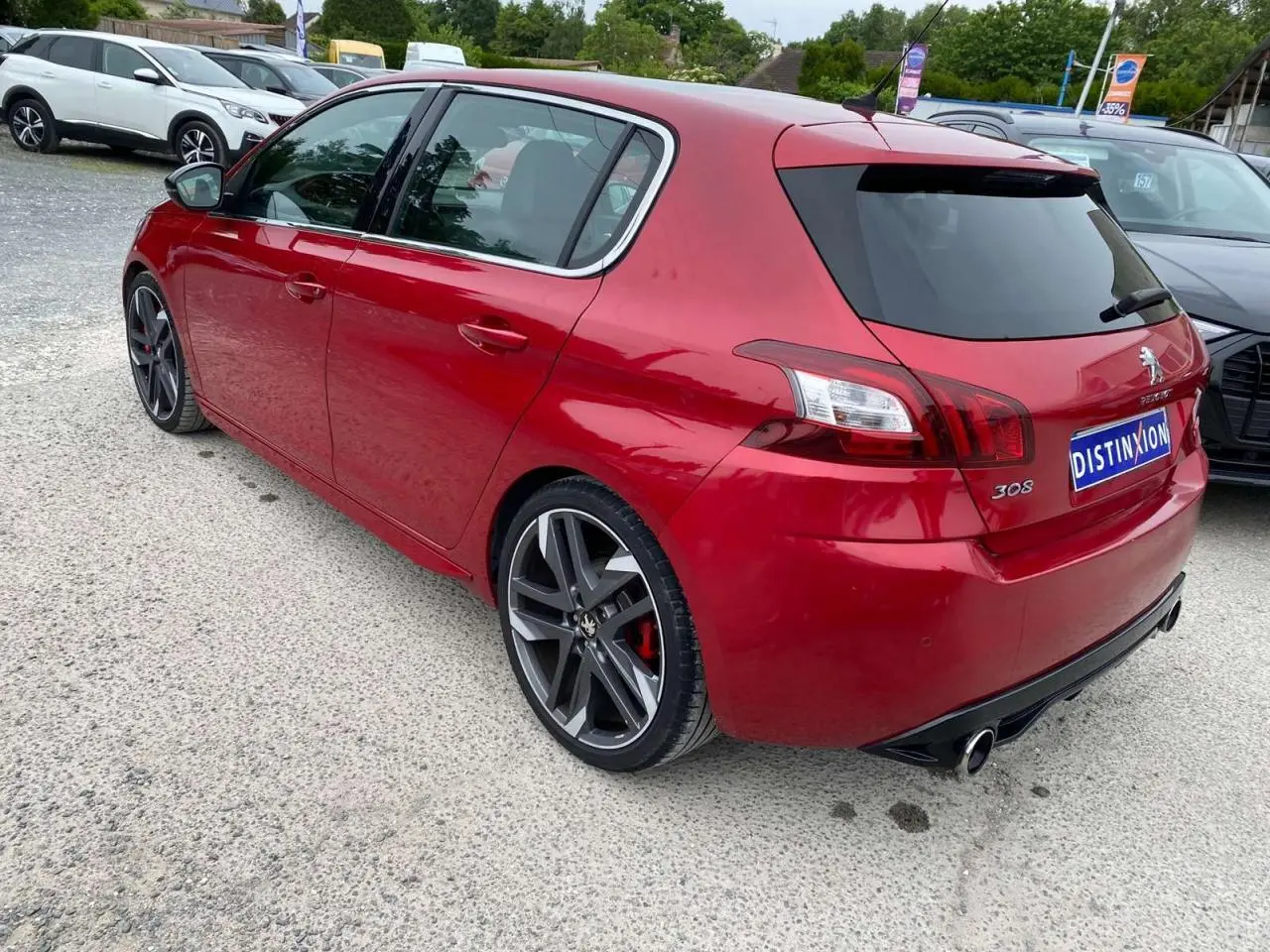 Vue 3/4 arrière droite d'une Peugeot 308 GTi rouge métallisée avec jantes sport et double sortie d'échappement.
