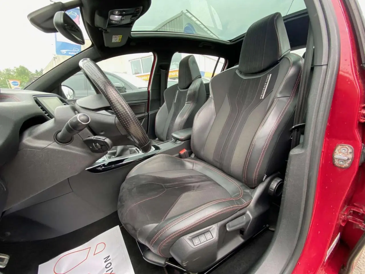 Intérieur avant droit de la Peugeot 308 GTi rouge 2016 avec sièges sport noirs et toit panoramique en verre.