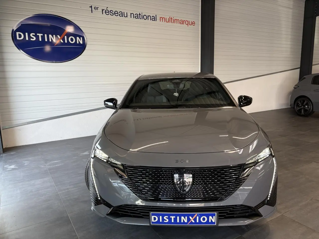 Vue de face d'une Peugeot 308 gris selenium avec calandre noire brillante et feux LED griffés dans un showroom