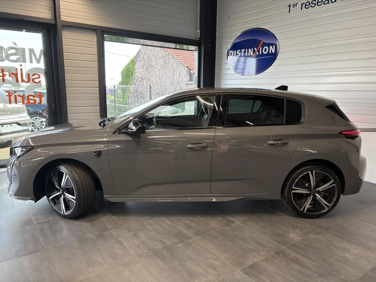 Profil côté gauche de la Peugeot 308 gris sélénium avec jantes alliage 18'' et vitres surteintées en showroom.