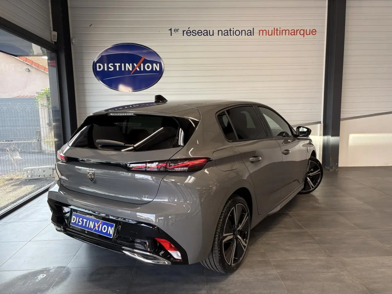 Vue 3/4 arrière droit d'une Peugeot 308 GT gris sélénium avec jantes alliage 18'' et bandeau noir brillant entre feux arrière.