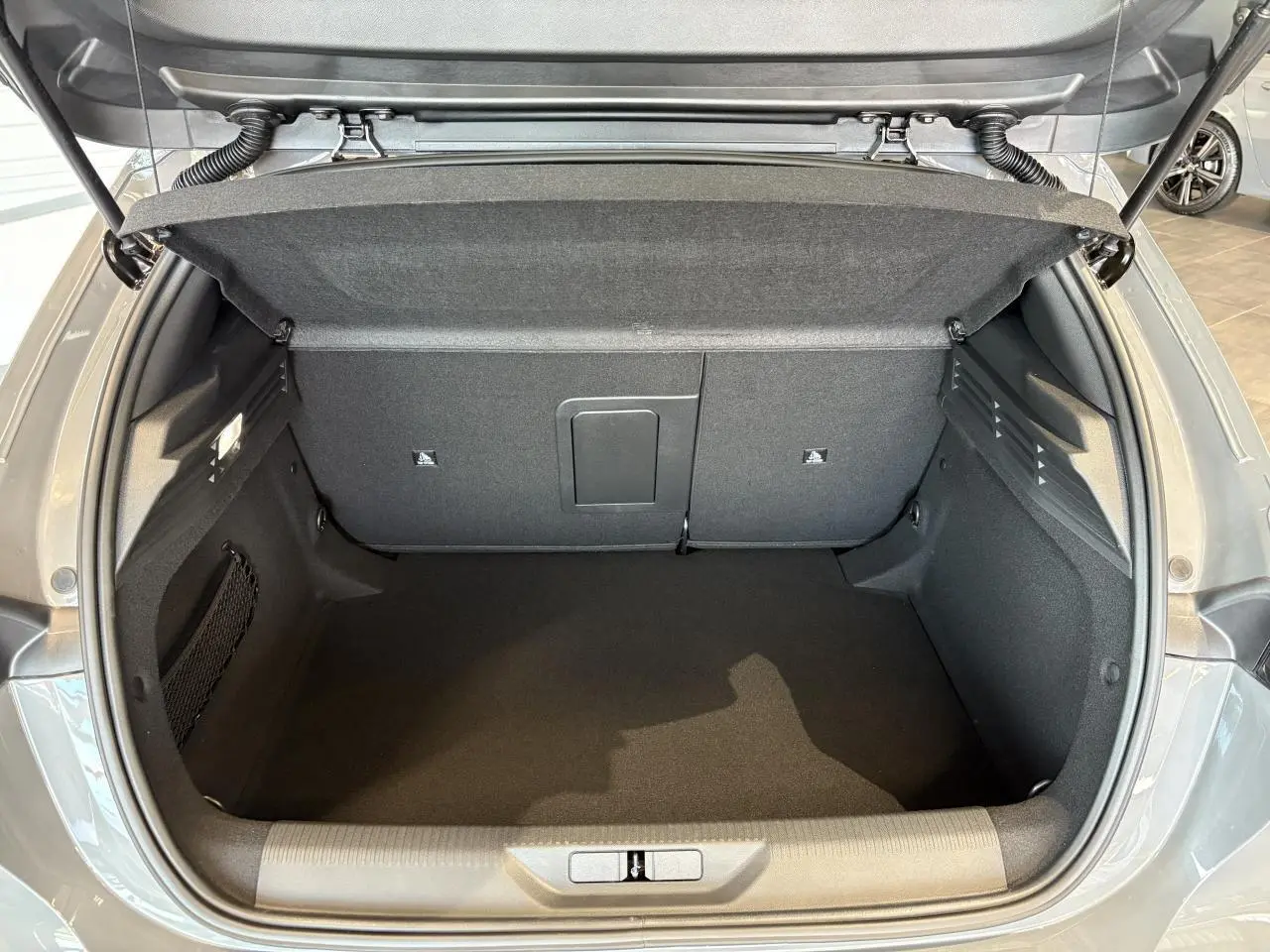 Coffre ouvert vu de l'arrière d'une Peugeot 308 gris selenium, montrant l'espace de chargement vide et propre.