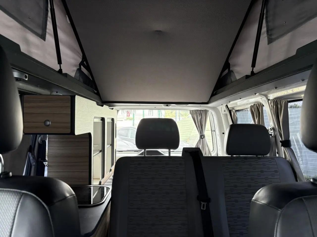 Intérieur du Volkswagen Transporter aménagé, vue arrière montrant sièges gris et rangements bois clairs.