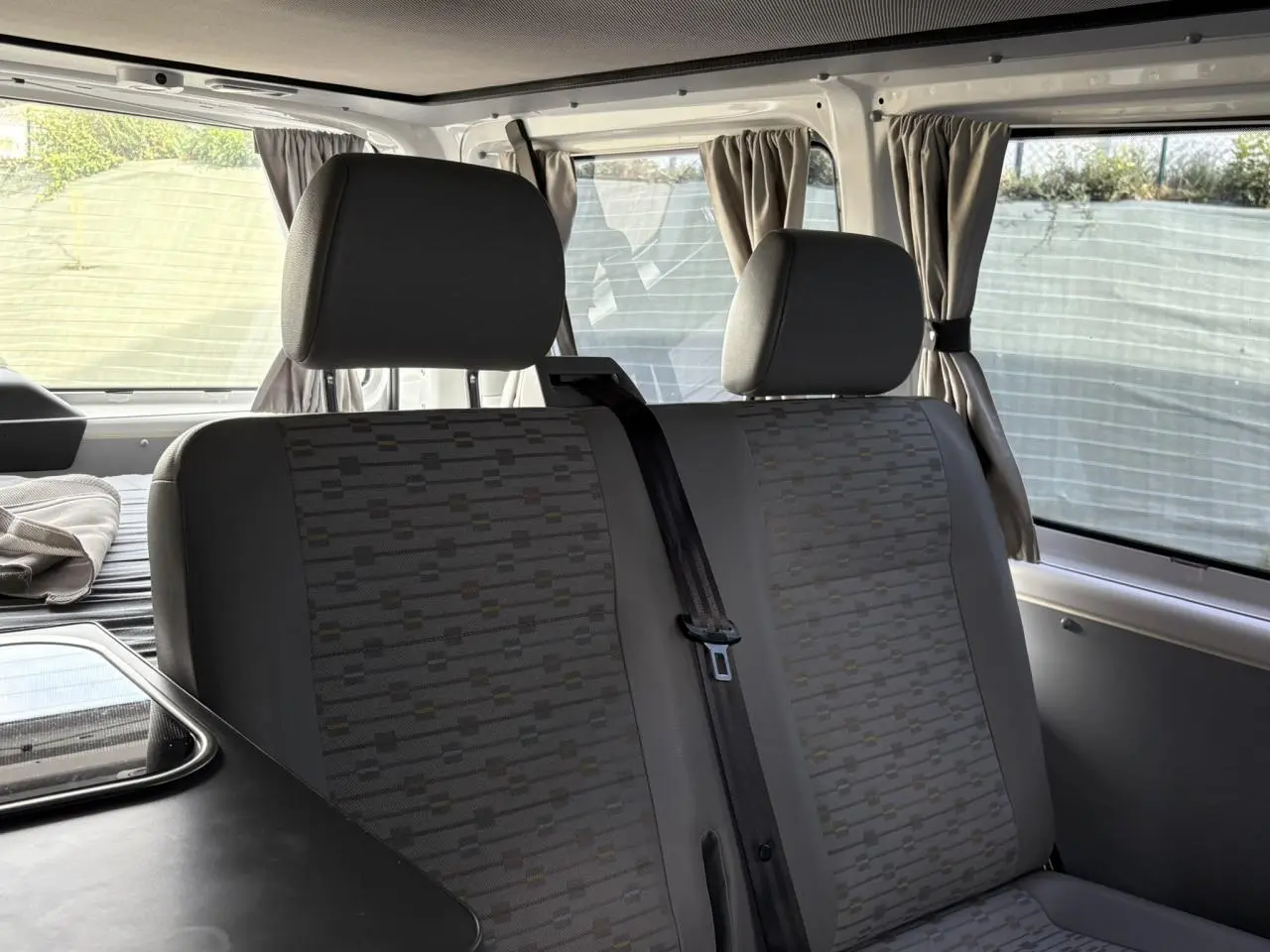 Vue intérieure du Volkswagen Transporter aménagé 2017, montrant les sièges arrière gris avec appuie-têtes et rideaux aux fenêtres.