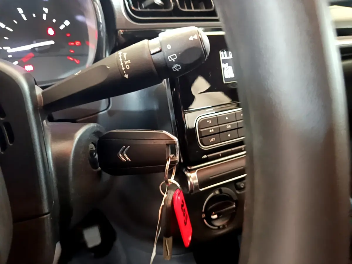 Vue rapprochée de l’intérieur côté gauche du volant noir d’une Citroën C3 blanche avec clé insérée et commandes au tableau de bord.