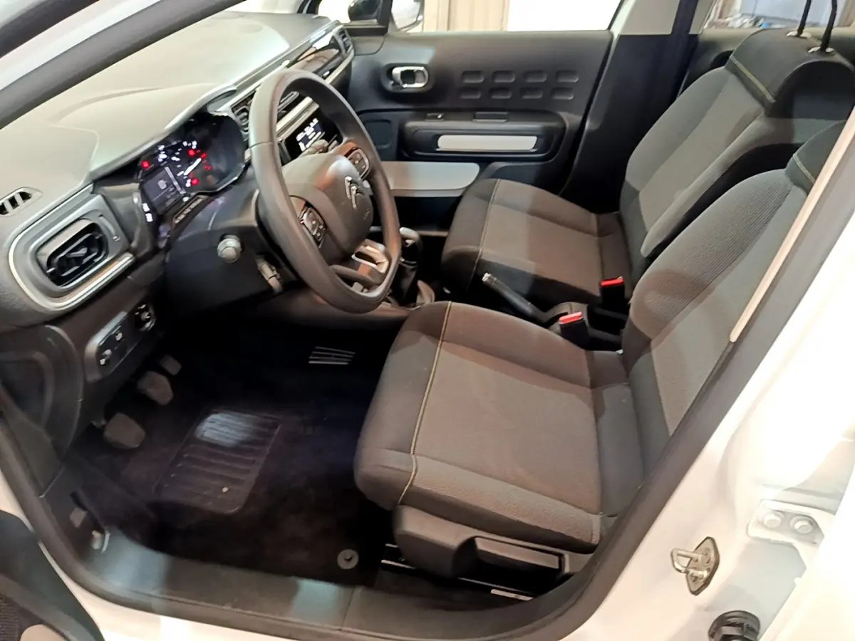 Vue intérieure côté conducteur de la Citroën C3 blanche 2018, sièges noirs et tableau de bord avec volant multifonctions.