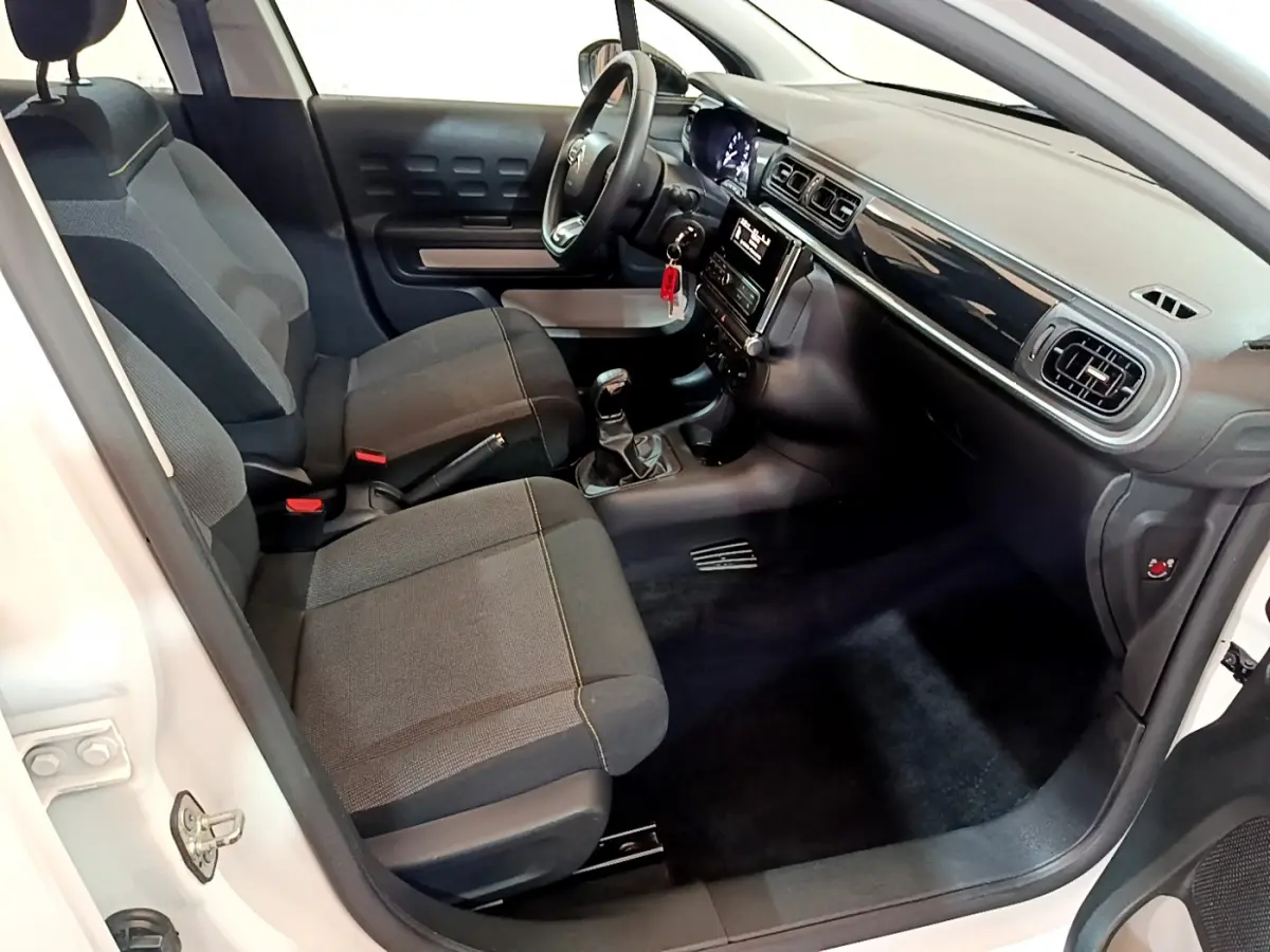 Intérieur avant de la Citroën C3 blanche 2018, vue côté conducteur montrant sièges tissu et tableau de bord noir brillant.