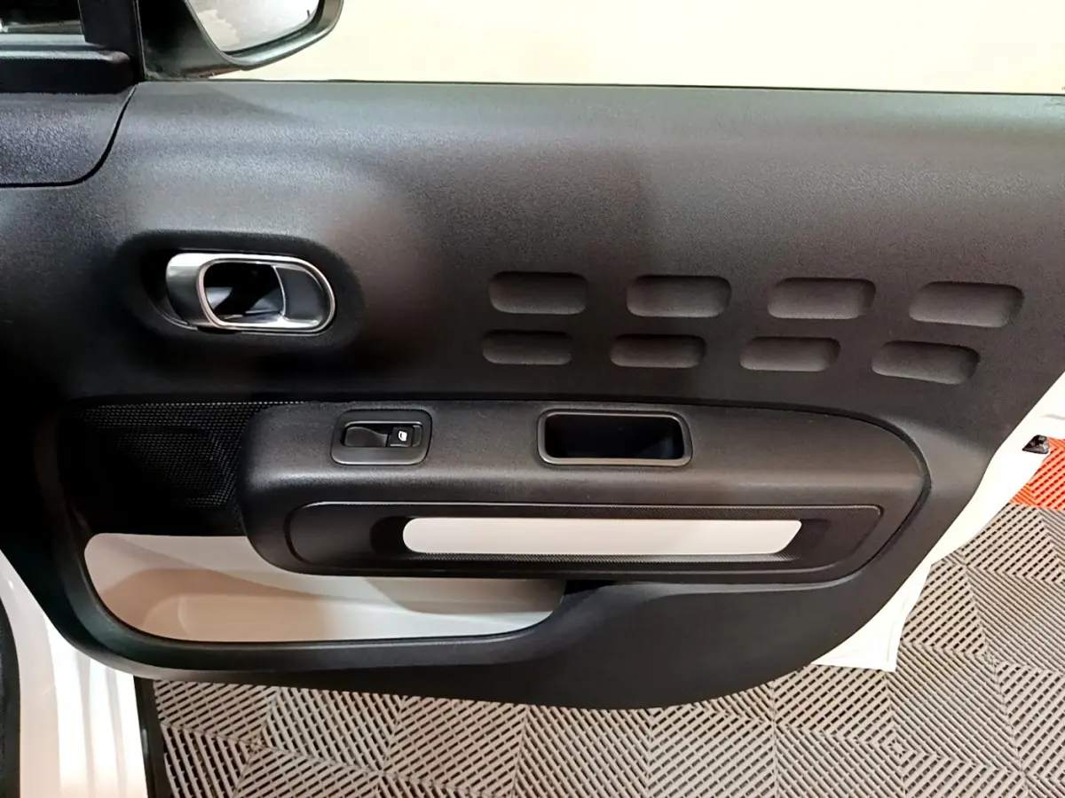 Vue rapprochée de la porte intérieure côté gauche blanche d'une Citroën C3 2018 avec poignée chromée et panneau noir texturé.