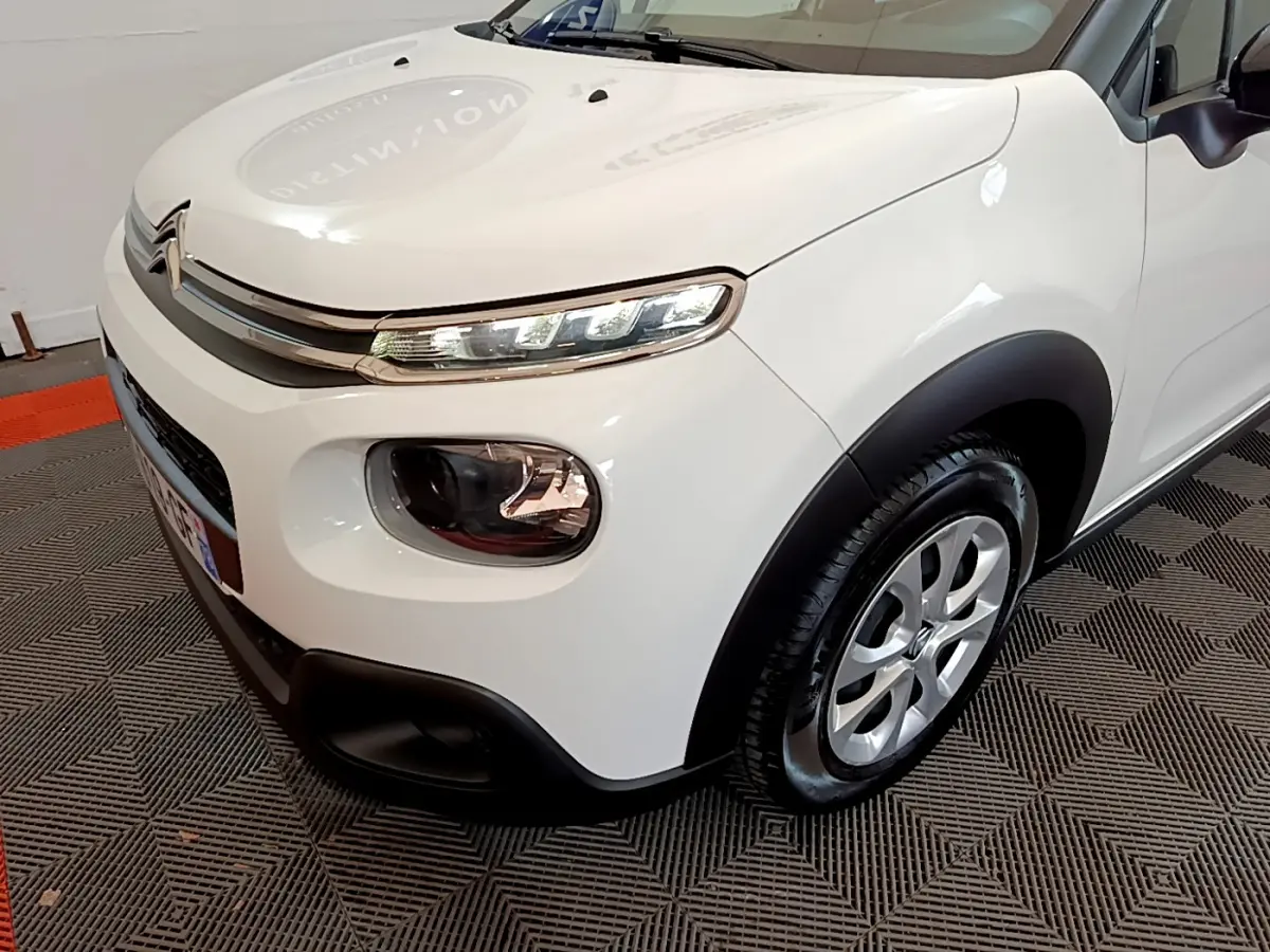 Vue 3/4 avant droit d'une Citroën C3 blanche de 2018 avec phares LED et protections noires sur les ailes.