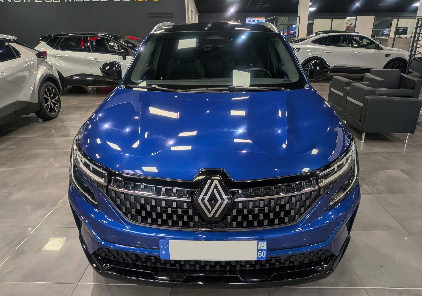 Vue frontale d'un Renault Austral E-Tech Hybrid 200 ch Iconic en Bleu Iron, avec calandre noire et logo central lumineux.