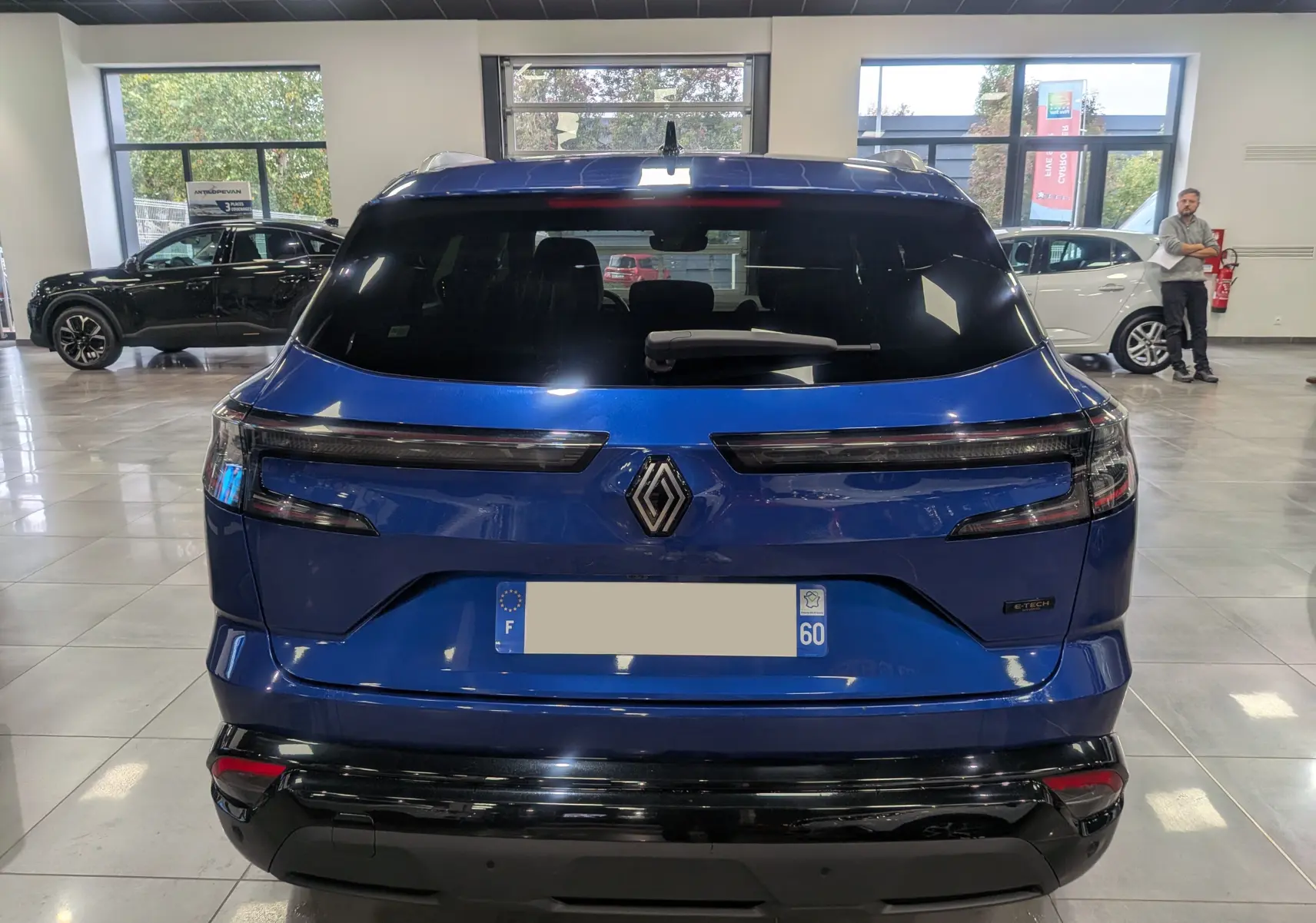 Vue arrière d'un Renault Austral E-Tech Hybrid bleu Iron en showroom, avec feux arrière LED et logo Renault central.