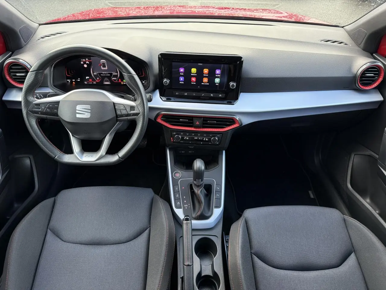 Vue intérieure frontale du tableau de bord du SEAT Arona rouge pur 2024 avec volant sport cuir Nappa et écran tactile central.