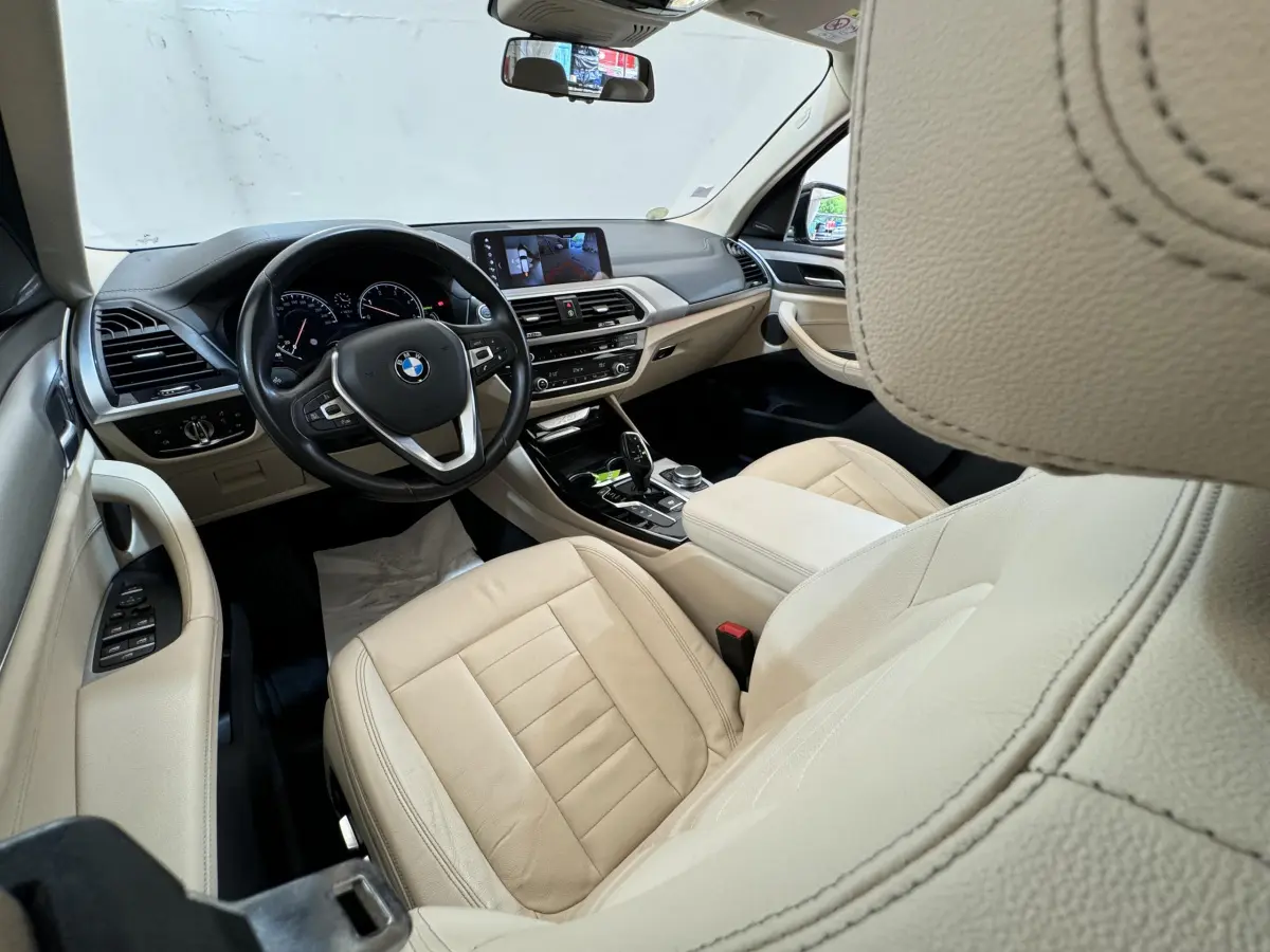 Vue intérieure côté conducteur de la BMW X3 2018 avec sièges cuir beige et tableau de bord moderne noir et beige.