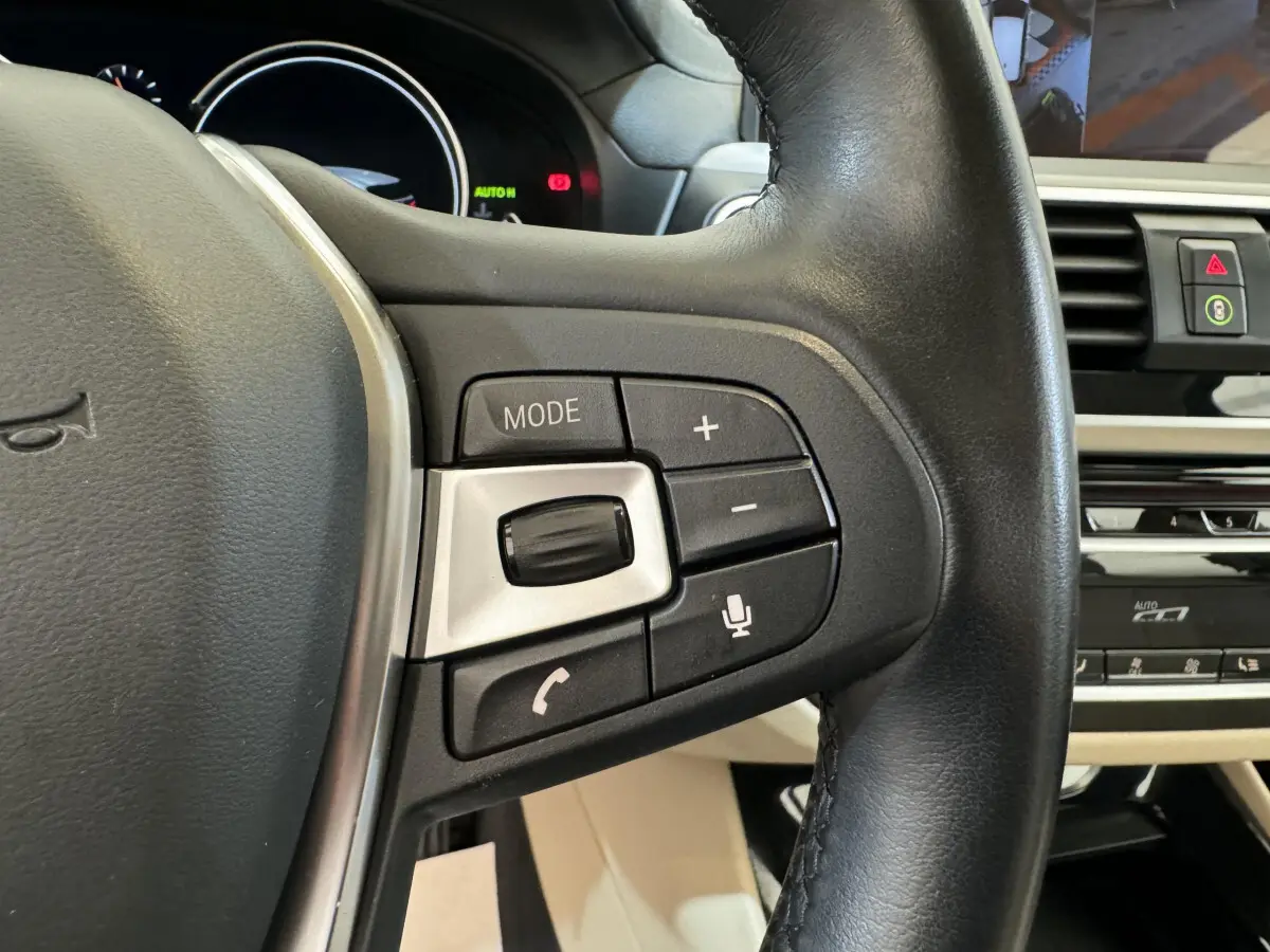 Gros plan sur les commandes multifonctions du volant cuir noir du BMW X3 xDrive30d 2018, tableau de bord en arrière-plan.