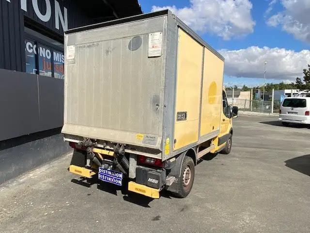 Vue 3/4 arrière droite d'un Ford Transit Chassis Cabine jaune avec caisse 12m3 et hayon, stationné en extérieur.