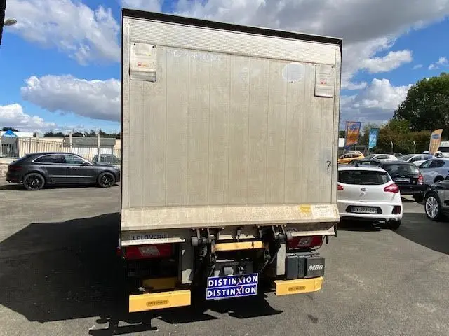 Vue arrière d'un Ford Transit Chassis Cabine jaune avec hayon élévateur, stationné en extérieur sous un ciel partiellement nuageux.