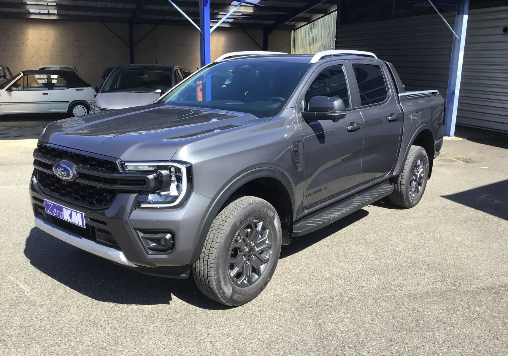 Ford Ranger Double Cabine gris carbone vu en 3/4 avant droit, avec marchepied et jantes alliage foncé.