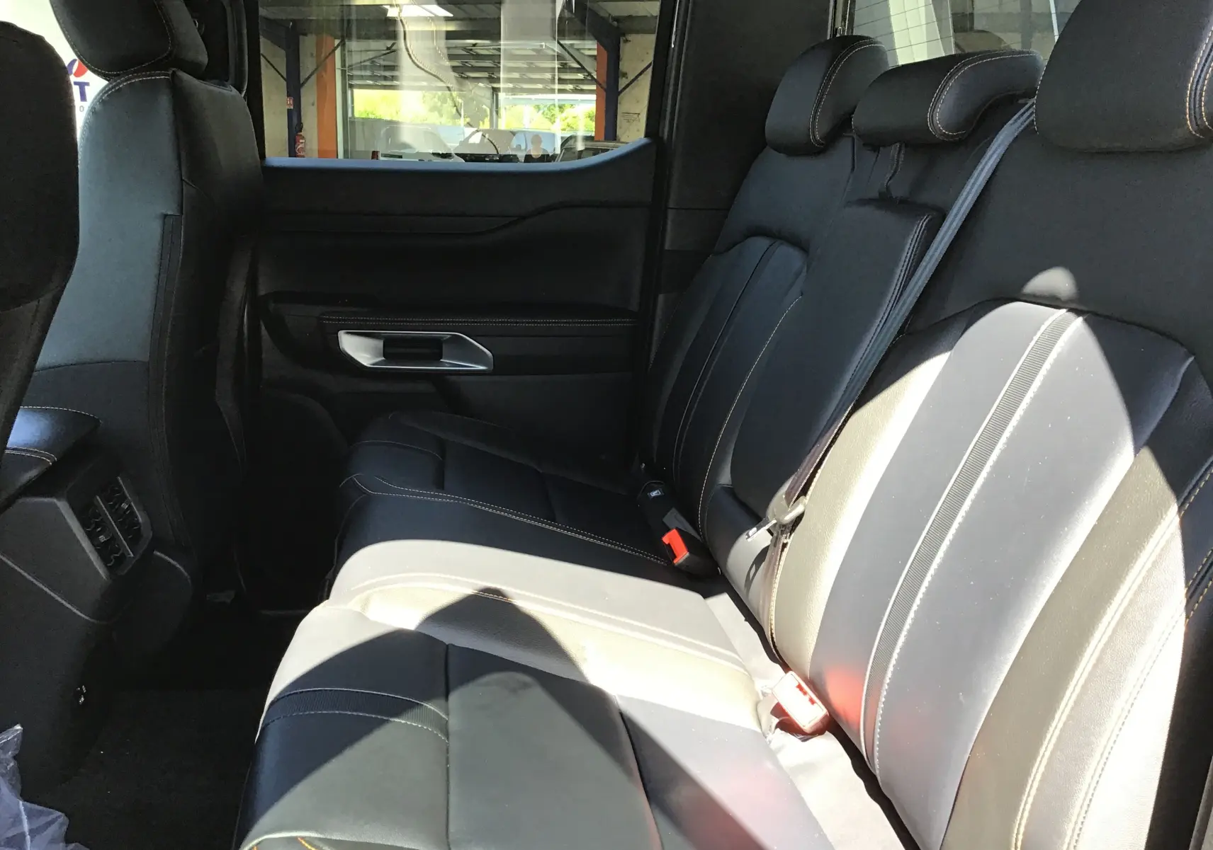 Vue latérale des sièges arrière en cuir noir avec surpiqûres orange du Ford Ranger Double Cabine gris carbone 2025.