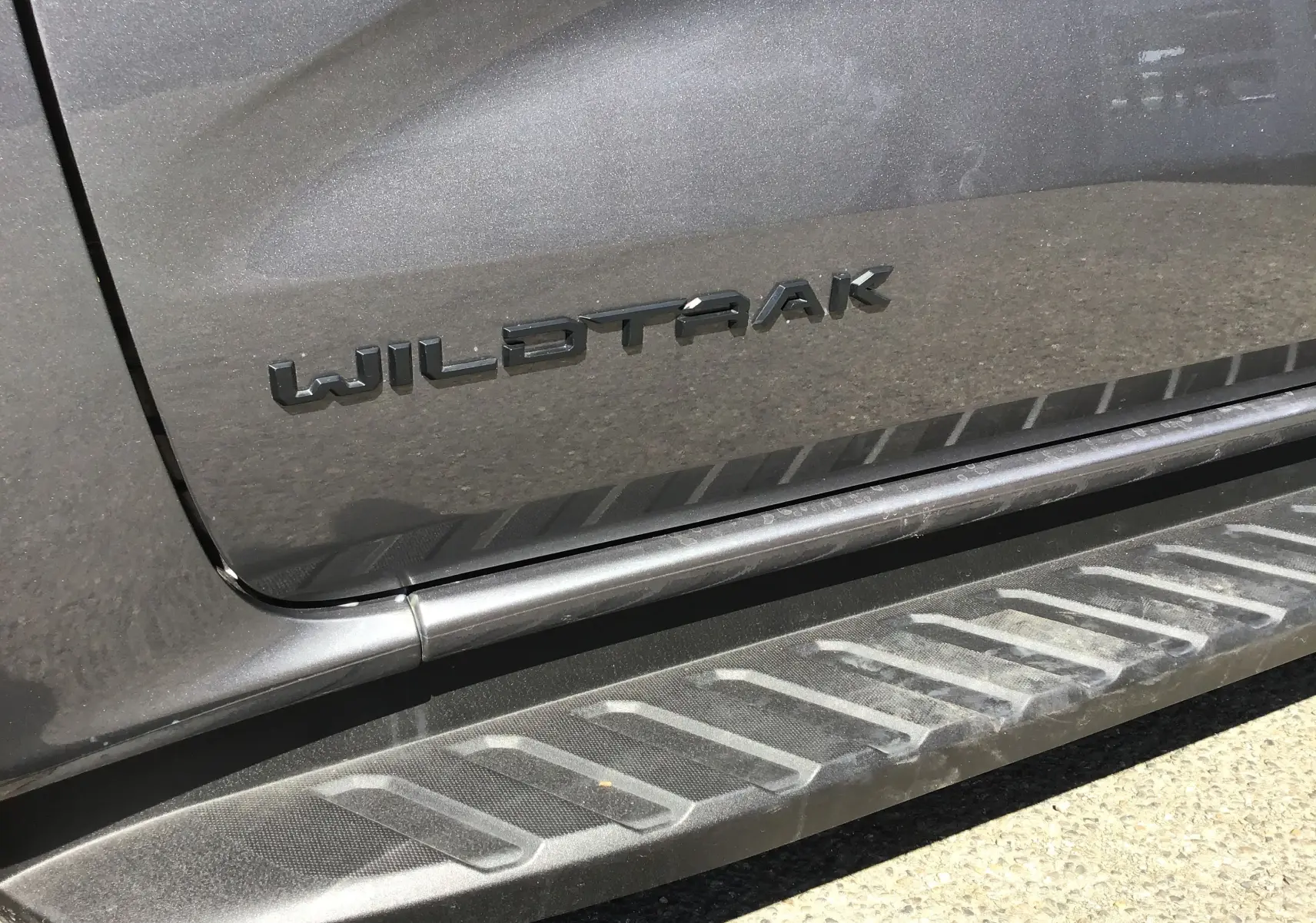 Gros plan sur la porte côté gauche gris carbone d'un Ford Ranger Wildtrak avec logo et marchepied texturé.