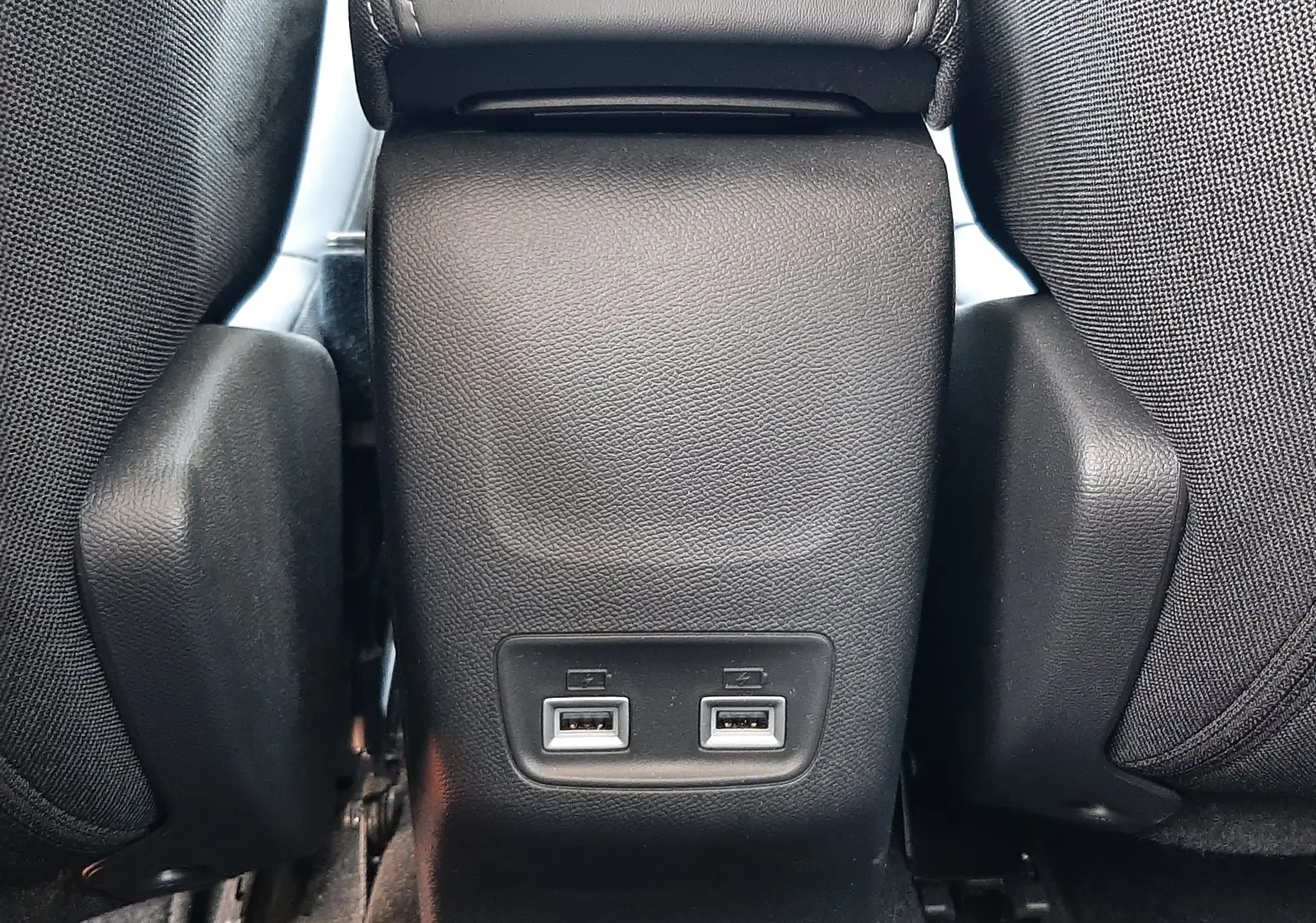 Vue rapprochée de la console centrale arrière noire du Peugeot 2008 gris Artense, avec deux ports USB visibles entre les sièges.