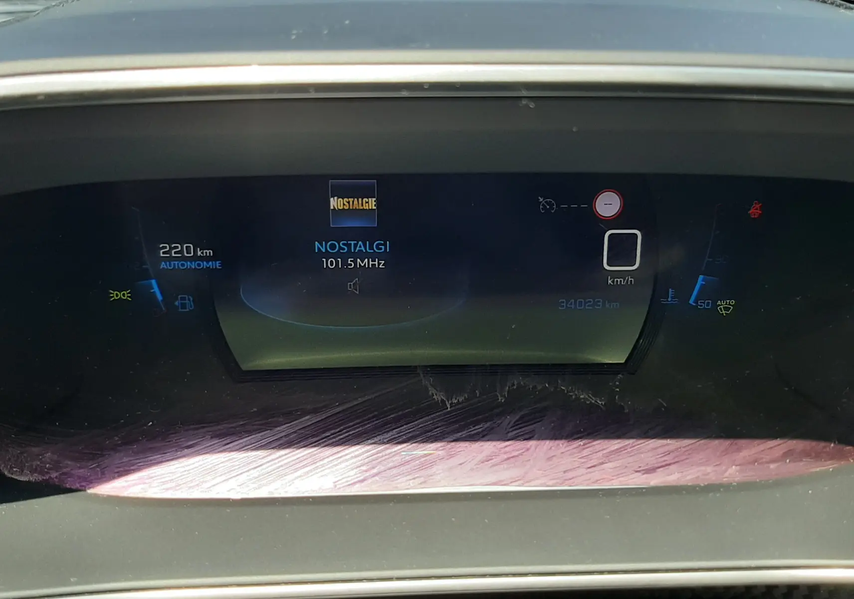 Tableau de bord numérique du Peugeot 2008 2022 affichant 220 km d'autonomie et la radio sur Nostalgie 101.5 MHz.