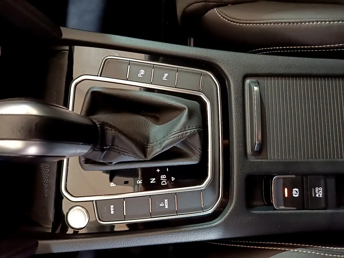 Gros plan sur la console centrale noire de la Volkswagen Passat hybride rechargeable, avec levier de vitesse automatique et boutons de contrôle.