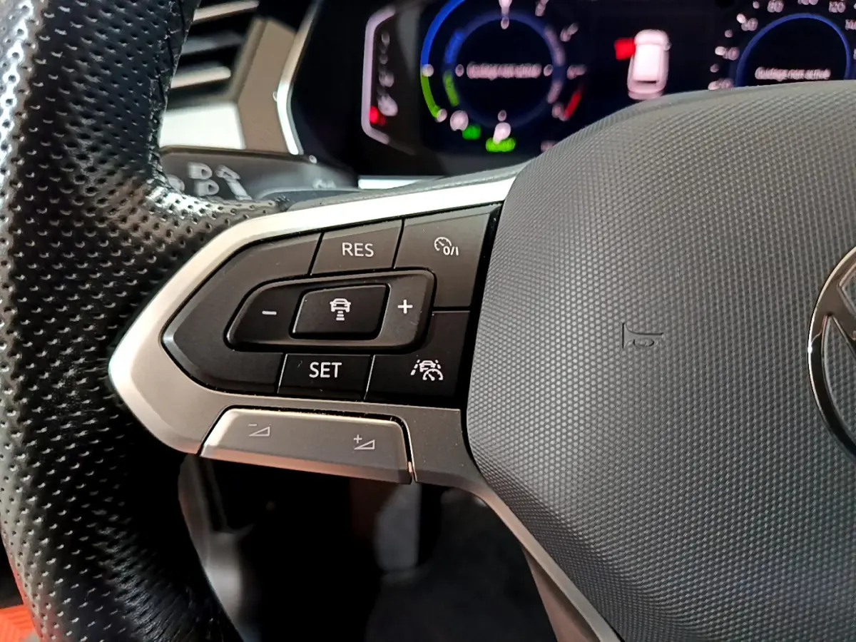 Gros plan sur les commandes du volant à gauche de la Volkswagen Passat hybride rechargeable 2022, avec tableau de bord numérique.