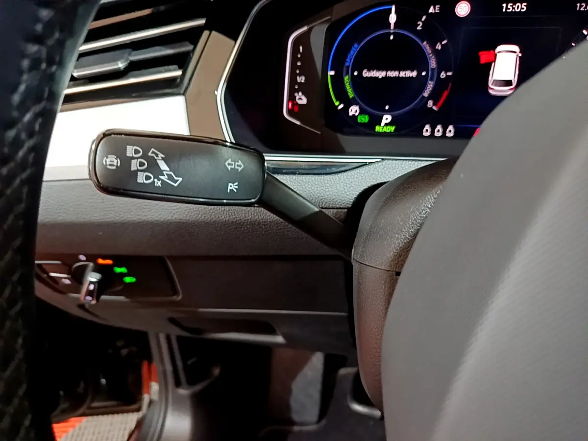 Gros plan sur la manette de clignotants à gauche du volant d'une Volkswagen Passat hybride rechargeable, tableau de bord numérique visible.