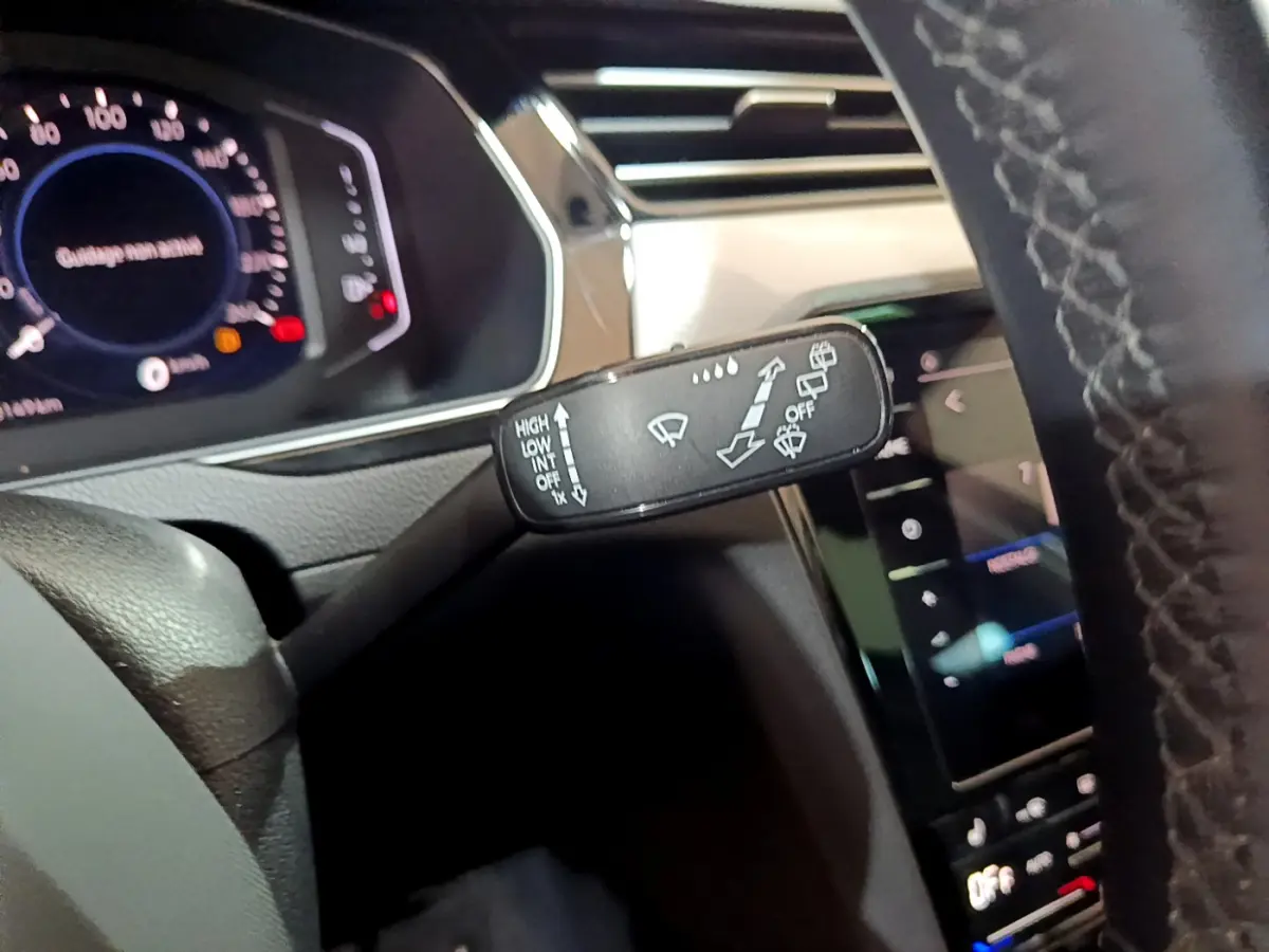 Gros plan sur la commande d’essuie-glace à gauche du volant dans l’habitacle gris foncé de la Volkswagen Passat hybride rechargeable 2022.