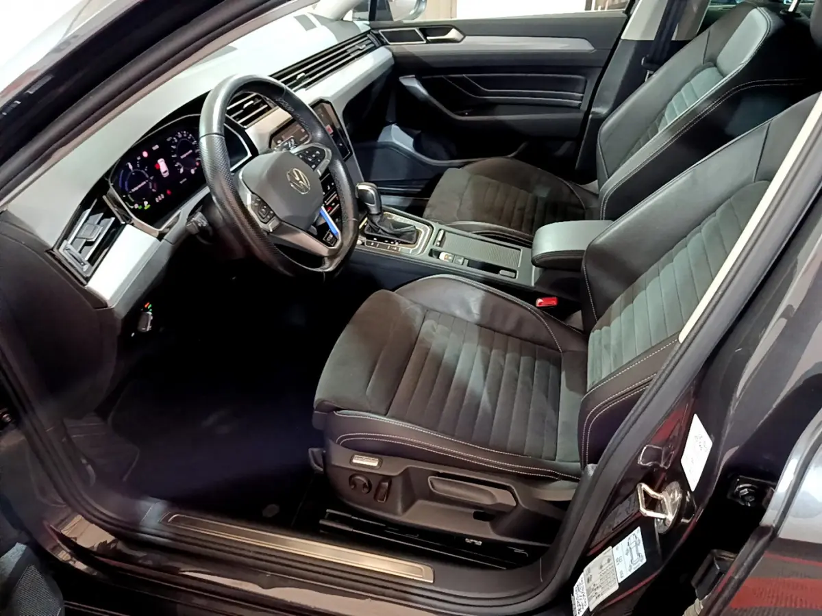 Vue intérieure côté conducteur de la Volkswagen Passat hybride rechargeable 2022, sièges noirs et tableau de bord digital.