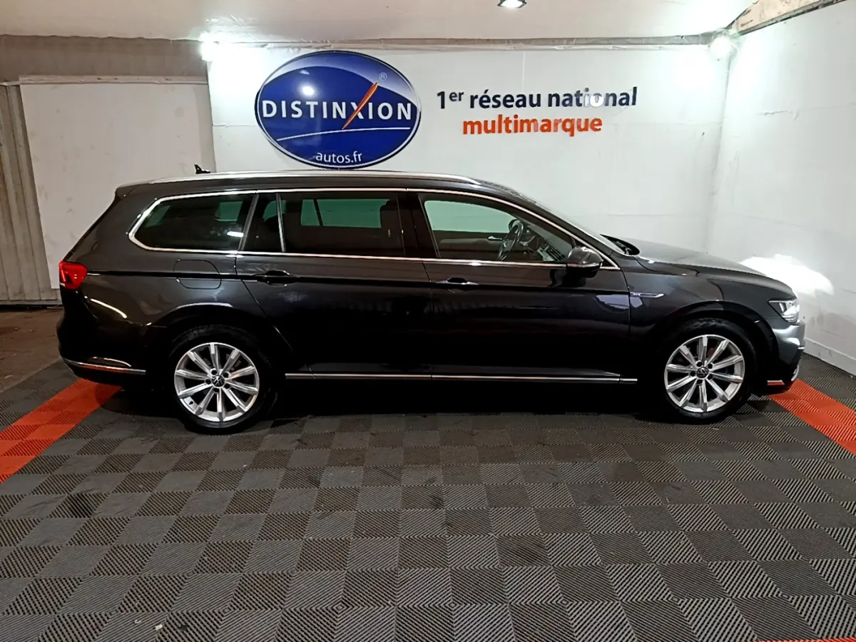 Profil droit d'une Volkswagen Passat SW GTE hybride rechargeable gris foncé dans un garage avec logo Distinxion en arrière-plan.