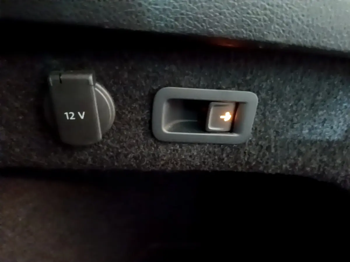 Prise 12V et bouton d'ouverture électrique du hayon dans le coffre de la Volkswagen Passat GTE hybride rechargeable gris foncé.