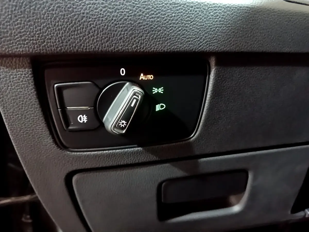 Gros plan sur le bouton de commande des phares avec réglage automatique dans l'habitacle noir de la Volkswagen Passat hybride.